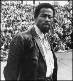Eldridge Cleaver, Ministro da Informação dos Panteras Negras, usando jaqueta de couro e olhando intensamente para a câmera durante um comício político.