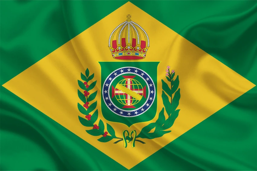 Bandeira do Brasil Império tremulando com efeito de tecido. A imagem mostra o fundo verde, o losango amarelo no centro e o brasão imperial brasileiro completo, incluindo a coroa, o escudo verde com o globo armilar e a Cruz da Ordem de Cristo, cercado por ramos de café e tabaco.
