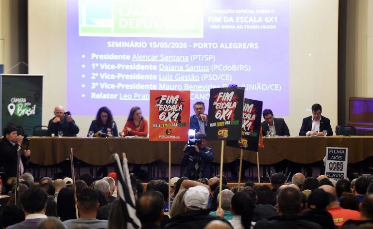 Debate sobre o fim da escala 6x1 na Câmara de Porto Alegre. A foto foi tirada do fundo da Câmara, onde é possível ver os populares com placas pedindo o fim da escala 6x1 e na mesa os parlamentares. Foto: Câmara dos Deputados.