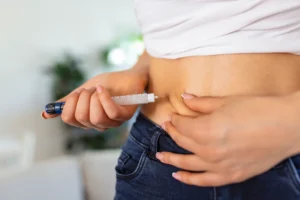 Close-up de uma pessoa aplicando medicamento na barriga, representando o uso de canetas emagrecedoras, como Mounjaro ou Wegovy.