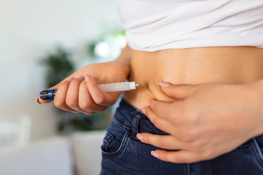 Close-up de uma pessoa aplicando medicamento na barriga, representando o uso de canetas emagrecedoras, como Mounjaro ou Wegovy.