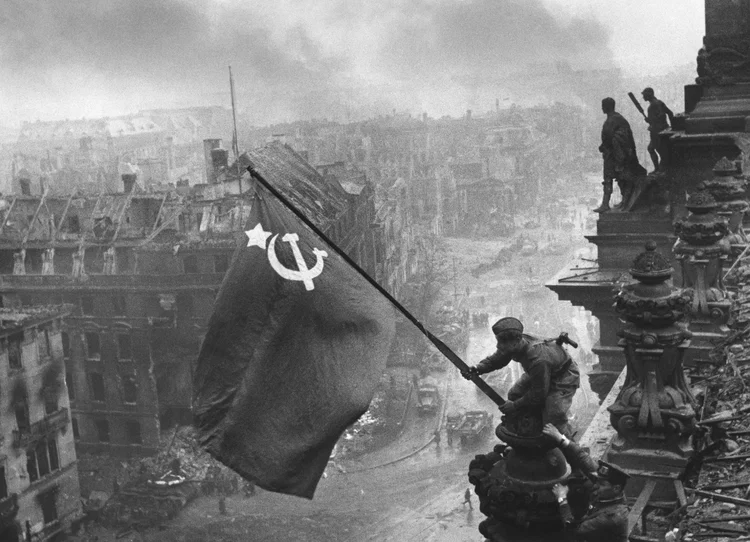 Soldado soviético hasteia a bandeira da União Soviética sobre o Reichstag, em Berlim, em meio à destruição causada pela Segunda Guerra Mundial.